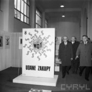 trzech mężczyzn w płaszczach w hali wystawowej