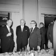 grupa stojących mężczyzn, przed nimi nakryty obrusem i zastawiony stół