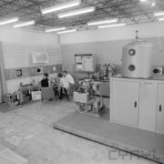 stoiska w hali wystawowej, w głębi dwie kobiety i mężczyzna siedzący na fotelach przy urządzeniu