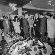 grupa kobiet i mężczyzn przy stoisku z butami w pawilonie wystawowym, pośrodku dwóch mężczyzn podaje sobie ręce