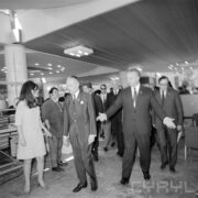 kobieta (z lewej) i grupa mężczyzn w pawilonie wystawowym