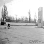 ulice na terenie targów, w głębi afisz z propagandowym hasłem, z prawej słup z propagandowymi hasłami