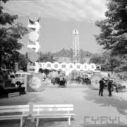 stoisko z samochodami i traktorami na betonowym placu, w głębi otynkowany budynek ze spadzistym dachem