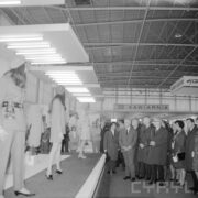 grupa kobiet i mężczyzn, część w płaszczach, w hali wystawowej