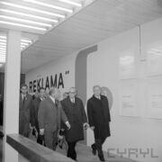 grupa mężczyzn, część w płaszczach, w hali wystawowej