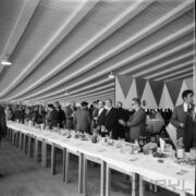 duża grupa mężczyzn stojących przy zastawionym stole w hali wystawowej