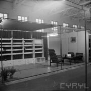 stoisko z meblami w hali wystawowej, z prawej trzy tapicerowane fotele, jeden z nich wyższym oparciem, mały stolik