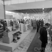 stoiska w pawilonie wystawowym, pomiędzy nimi zwiedzający ludzie