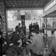 kobiety i mężczyźni w pawilonie wystawowym, część z nich siedzi, część stoi