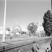 pośrodku ażurowa konstrukcja z kulą ziemską,w głębi maszty z flagami państw, z przodu prostokątna fontanna i kwietniki