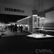 stoiska w pawilonie wystawowym, między nimi zwiedzający ludzie