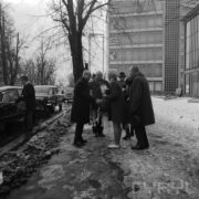 grupa kobiet i mężczyzn, stojących na ośnieżonym chodniku, część osób podaje sobie ręce, z lewej stoją zaparkowane samochody