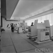 stoisko z kuchenkami gazowymi w pawilonie wystawowym, między nimi zwiedzający ludzie