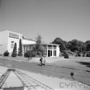 pawilon wystawowy z półokrągłym wejściem, przy pawilonie drzewa i krzewy, spacerujący ludzie