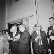 grupa kobiet i mężczyzn, część z nich trzyma w rękach miseczki, jedzą, część mężczyzn kieliszki