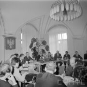 grupa mężczyzn siedzi przy stole, ustawionym w kształcie litery U