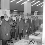 grupa ludzi, część w płaszczach w hali wystawowej