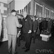 grupa mężczyzn w hali wystawowej, na pierwszym planie dwóch mężczyzn podaje sobie ręce