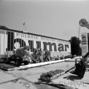 samochody budowlane i urządzenia na betonowym placu, tle dużego napisu z nazwą Bumar