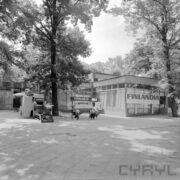 przeszklony pawilon wystawowy, otoczony drzewami, przed nim wystawa urządzeń