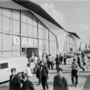 przeszklony budynek, przed budynkiem zwiedzający ludzie i zaparkowane samochody