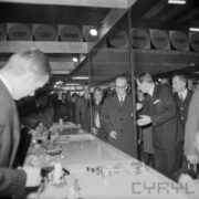 grupa ludzi w płaszczach w hali wystawowej