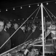 grupa mężczyzn w płaszczach w hali wystawowej