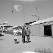 dwie kobiety i mężczyzna na terenie wystawy, za nimi dwa zaparkowane koło siebie autobusy, z prawej fragment hali wystawowej