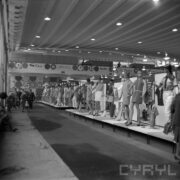 stoiska z ubranymi manekinami w hali wystawowej, z lewej w głębi grupa zwiedzających osób