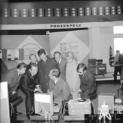 kilku mężczyzn, część z nich pochylona, i jedna kobieta przy stoisku wystawowym