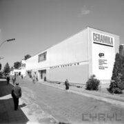 murowany budynek, stojący wzdłuż ulicy na terenie targów, ulicą spacerują ludzie