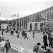 przeszklony budynek, przed nim spacerujący ludzie