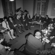 grupa mężczyzn i kobiet siedząca przy stołach, na stołach szklanki, kieliszki, butelki i talerze