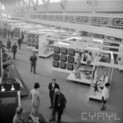 stoiska z ubranymi manekinami w hali wystawowej, pomiędzy stoiskami ludzie