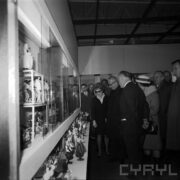 grupa kobiet i mężczyzn ogląda stoisko z figurkami w strojach ludowych