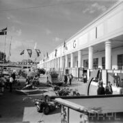 stoiska z maszynami i urządzeniami, z lewej budynek z podcieniami i kolumnadą wzdłuż budynku, zwiedzający ludzie