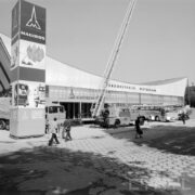 przeszklona hala wystawowa z wklęsłym dachem, przed halą stoiska z samochodami dla straży pożarnej, spacerujący ludzie