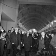 grupa ludzi w płaszczach w hali wystawowej