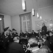 grupa mężczyzn i kobiet siedząca przy stołach, na stołach szklanki, kieliszki, butelki i talerze