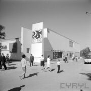 murowany, otynkowany budynek, spacerujący ludzie, z prawej samochód osobowy