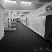 z lewej stoiska z ubranymi manekinami w hali wystawowej, z prawej w gablotach wywieszone ubrania