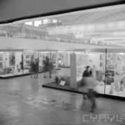 stoiska w hali wystawowej, pomiędzy nimi kilkoro ludzi, postacie niewyraźne, zamazane