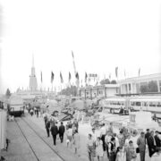 ulica z torami kolejowymi na terenie wystawy, dookoła budynki wystawowe, spacerujący ludzie