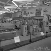 stoisko z urządzeniami w hali wystawowej, między nimi zwiedzający ludzie