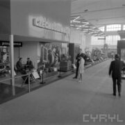 stoisko z urządzeniami w hali wystawowej, między nimi zwiedzający ludzie