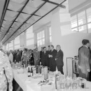 duża grupa ludzi stojąca przy zastawionych stołach w hali wystawowej