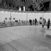 stoisko w hali wystawowej, zwiedzający ludzie, u sufitu wiszą okrągłe reklamy firm