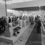 stoiska w pawilonie wystawowym, pomiędzy nimi zwiedzający ludzie