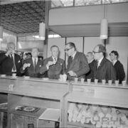 grupa mężczyzn stoi przy ladzie na której ustawiono z prawej  papierowe kubki, część z mężczyzn trzyma w rękach filiżanki