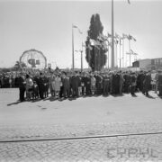 duża grupa ludzi stoi na terenie targów, za nimi ażurowa konstrukcja kuli ziemskiej i maszty z flagami państw